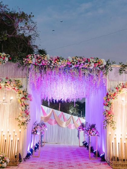 A breathtaking entrance for an unforgettable night. This grand entryway, with cascading wisteria, floral arches, and dramatic purple uplighting, set a magical tone for Melvin and Marilyn's reception from the moment guests arrived.