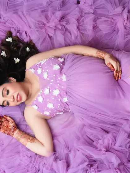 Dreaming of you. This overhead shot captures the mother-to-be lying on a bed of purple tulle, her hair adorned with flowers. It's a romantic and artistic perspective.