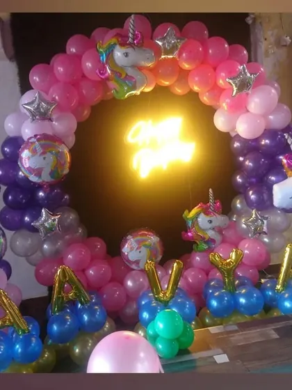 A magical unicorn-themed birthday party. The decoration includes a balloon arch with pink and purple colors, unicorn foil balloons, and the birthday girl's name in balloons.
