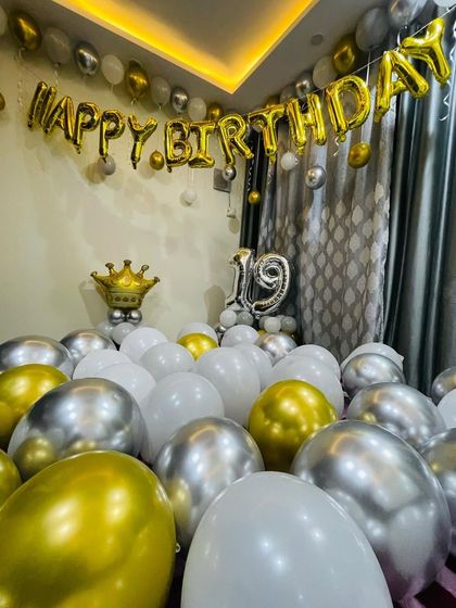 A 19th birthday celebration at home. The room is filled with gold, silver, and white balloons, with "Happy Birthday" and number foils on the wall.