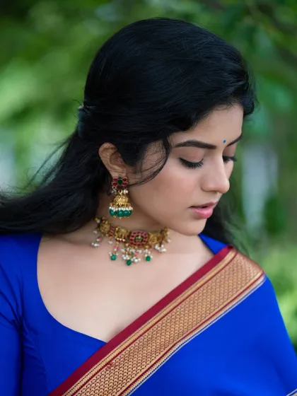 A close-up of Megha Shetty, focusing on her serene expression and the traditional jewelry that complements her blue saree.