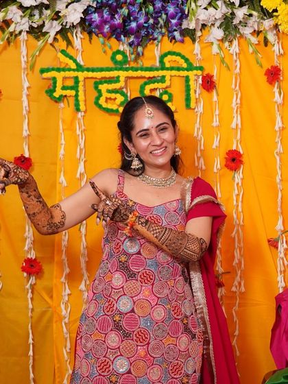 A happy, playful moment from an intimate home mehendi. The bride is wearing a colorful red sharara set, a comfortable and festive choice for the long hours of getting her henna done.