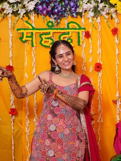 A happy, playful moment from an intimate home mehendi. The bride is wearing a colorful red sharara set, a comfortable and festive choice for the long hours of getting her henna done.
