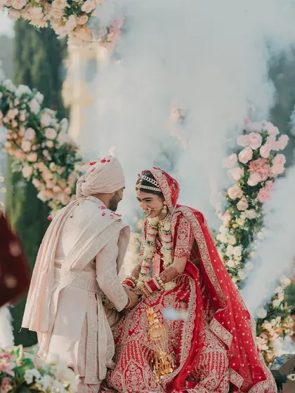 A romantic Varmala moment, with the couple looking into each other's eyes, enveloped in a gentle cloud of smoke under a floral arch.