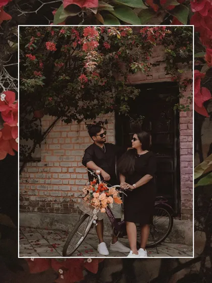 A romantic portrait of the couple with a bicycle adorned with flowers, framed by red bougainvillea.