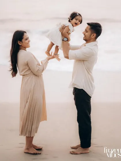 A full-length portrait of a family on the sand. The father holds their baby up as the mother reaches out, creating a beautiful, balanced composition that feels both posed and natural.