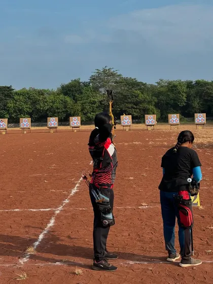 An archer prepares to take her shot, with the long line of targets visible in the background at the state competition.
