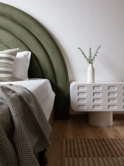 A detail of the custom white nightstand with carved patterns, set against the green velvet headboard. The design is a blend of playful forms and sophisticated details.