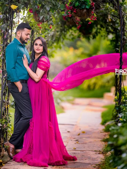 A classic romantic portrait set in a lush garden archway. The way the vibrant pink of her gown flows creates a sense of movement and life, perfectly complementing the couple's serene and stylish pose.