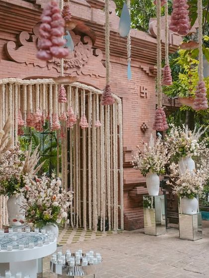 The entrance to this wedding combines a rustic brick facade with soft, romantic floral decor, including hanging pink floral tassels and abundant white flower arrangements.