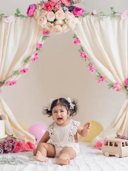 A candid, happy moment during her first birthday celebration. The soft drapes, floral garlands, and gentle lighting create a perfect setting for capturing a baby's joyful spirit.