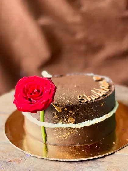 A rich chocolate cake made elegant with a single, perfect red rose and a sprinkle of gold dust.