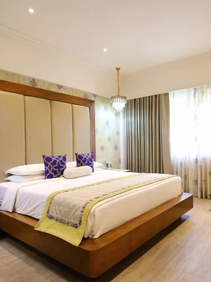 This suite at Vivanta Bengaluru features a large, statement headboard and pops of purple and yellow. The design blends modern comfort with luxurious details like crystal chandeliers and patterned wallpaper.