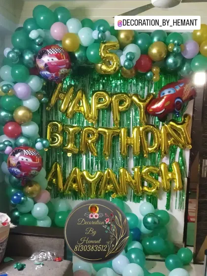 A car-themed birthday decoration for Aayansh's 5th birthday. This setup, perfect for a home celebration, features a green shimmer curtain and a dense balloon arch with Lightning McQueen foil balloons.