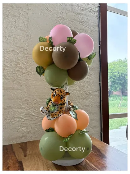 A jungle-themed balloon centerpiece with a small plush leopard, using a palette of green, brown, and pink.
