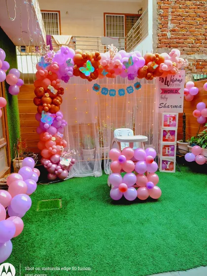 An outdoor welcome party for a baby, with a balloon arch and "BABY" blocks set up on an artificial grass lawn.