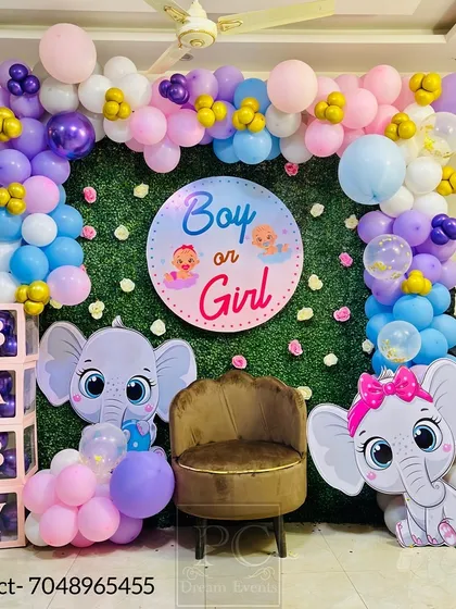A "Boy or Girl" gender reveal party setup with a baby elephant theme. A lush green wall is the base for a colorful balloon frame, cute elephant cutouts, and 'BABY' blocks.
