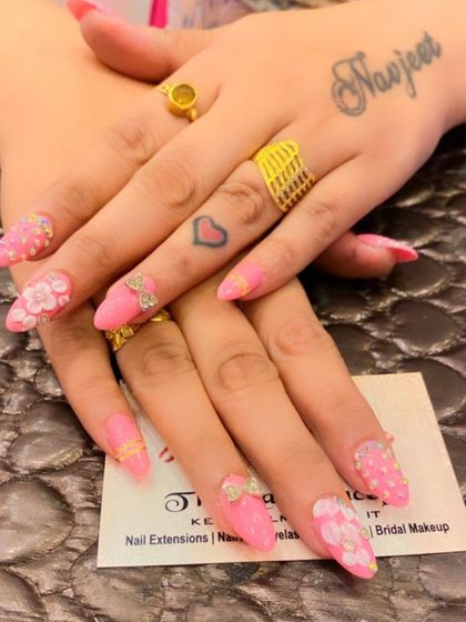 An incredibly detailed and feminine set of long, pink stiletto nails. The design includes 3D sculpted flowers, bows, and a variety of rhinestone and pearl embellishments.
