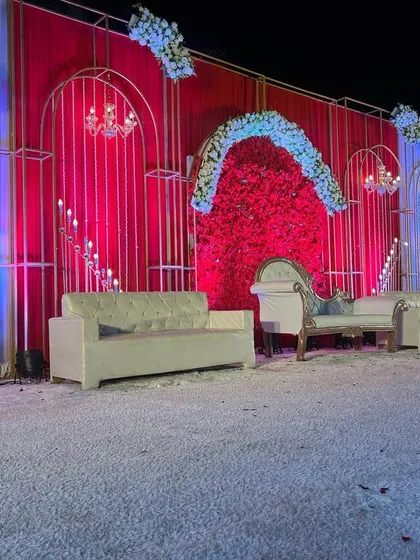 A wider view of the opulent all-red wedding stage. The combination of red drapes, a red flower wall, and white floral arches creates a multi-dimensional and luxurious look.