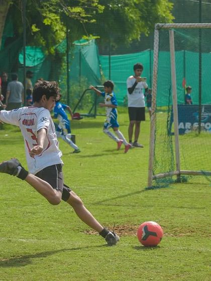 A player takes a powerful shot on goal with the goalkeeper ready to make a save, capturing a key moment of attack versus defense.