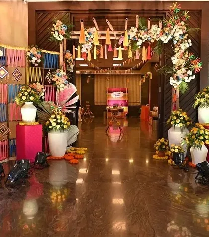 A colorful and traditional entrance for a Haldi ceremony. The decor features woven wall hangings, marigold arrangements in white vases, and a personalized welcome easel.