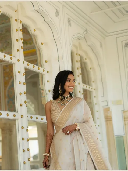 A joyful, candid portrait of Vedika in a beautiful white and gold saree. Her genuine smile and the elegant backdrop of a Rajasthani palace make this a radiant shot.