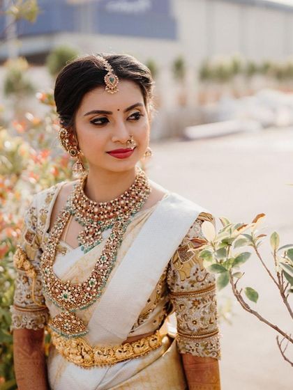 A bride posing in a garden, her white and gold saree looking ethereal in the soft light.
