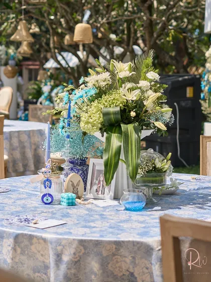 A guest table with a blue and white patterned tablecloth, a large floral centerpiece, and various themed trinkets.