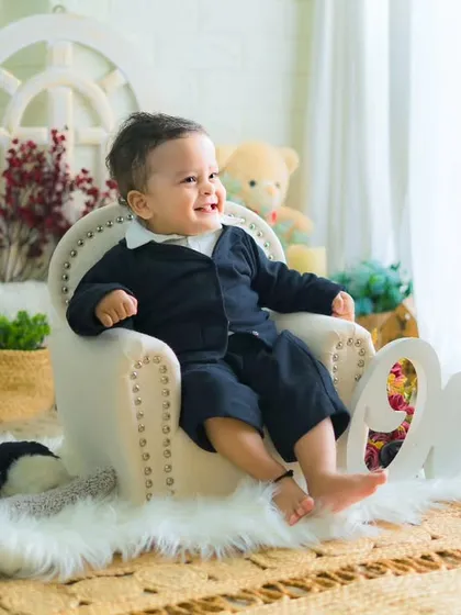A classic and joyful first birthday portrait. This little boy in his smart suit is all smiles, sitting in a miniature armchair in a beautifully lit studio.