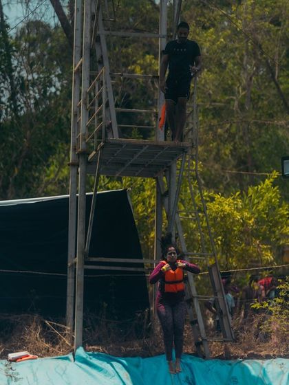 A participant practices a compact jump from the diving platform under supervision. This technique is vital for minimizing impact when falling from the 25 foot wall.