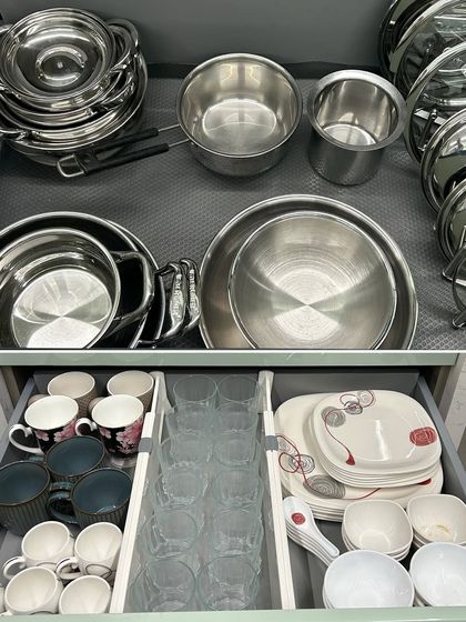 A two-tiered view of organized drawers. The top holds steel cookware, while the bottom has everyday mugs, glasses, and plates sorted with dividers.