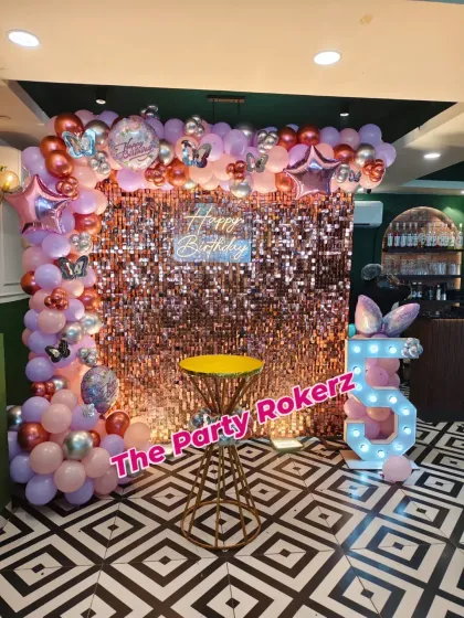 This butterfly party setup features a stunning rose gold sequin wall. The balloon arch in shades of purple, pink, and silver, along with the light-up number '5', creates a glamorous photo opportunity.