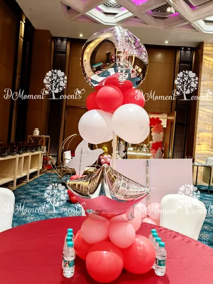 A table centerpiece for a multi-themed party, featuring red and white balloons with silver star and orb accents.