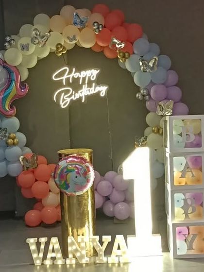 A magical unicorn theme for Vanya's first birthday, featuring a circular backdrop, neon sign, and pastel rainbow balloons.