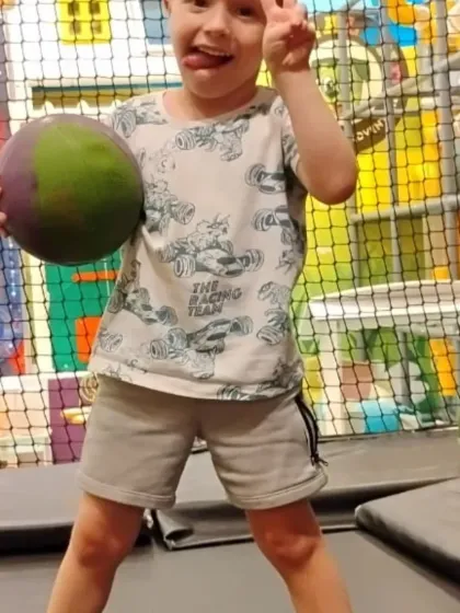 A boy shows off his playful side while balancing on the trampoline with a ball.