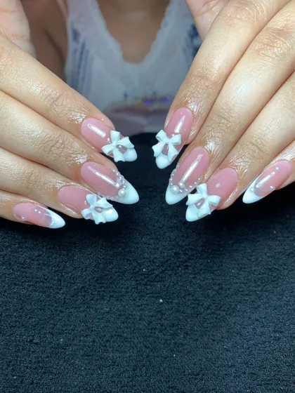 A classic French manicure gets an upgrade with 3D sculpted bows. This elegant design features white tips on almond-shaped nails, accented with delicate bows and pearls for a bridal or special occasion look.