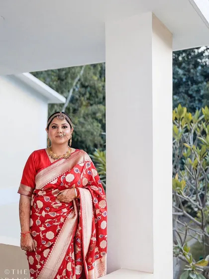 A full-length view of our bride in her traditional red saree. We styled her with a classic updo and a maang tikka, creating a look of timeless elegance for her wedding day.