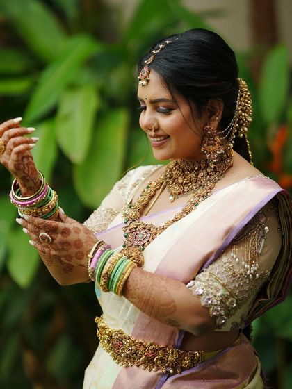 A bride adjusts her bangles, her hands adorned with henna. The soft colors of her saree and the delicate embroidery on her blouse create a beautiful picture.
