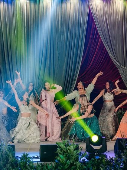 The bride's squad takes the stage for a joyful performance. The backdrop of dramatic, layered velvet drapery, inspired by Raja Ravi Varma's art, provides a rich and theatrical setting for the sangeet performances.