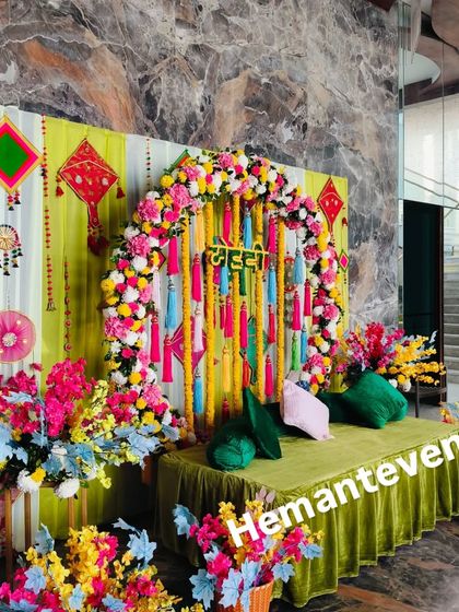A close-up of a colorful Mehendi backdrop. The floral arch and traditional hangings against the lime green seating create a perfect photo spot.