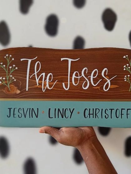 Two hands presenting the finished name plaque for "The Joses." This shows the scale and beautiful finish of our handcrafted wooden signs.