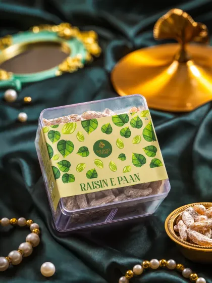 A package of Raisin-e-Paan, styled with green satin fabric and decorative props to match the paan leaf theme.