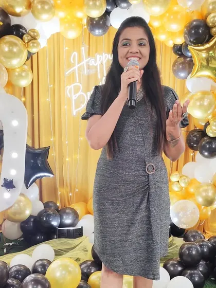 On stage at a 50th birthday party, with a beautiful black and gold balloon decor behind me. The right theme and decor really elevate a milestone celebration.