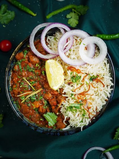A top-down shot of a hearty bowl of chana masala and rice. The fresh garnishes and dark, moody background make the dish look rich and flavorful.