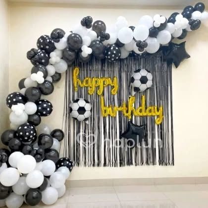 A cool football-themed birthday decoration. The black and white balloon arch is paired with a black shimmer curtain, football-shaped balloons, and 'Happy Birthday' foil letters.