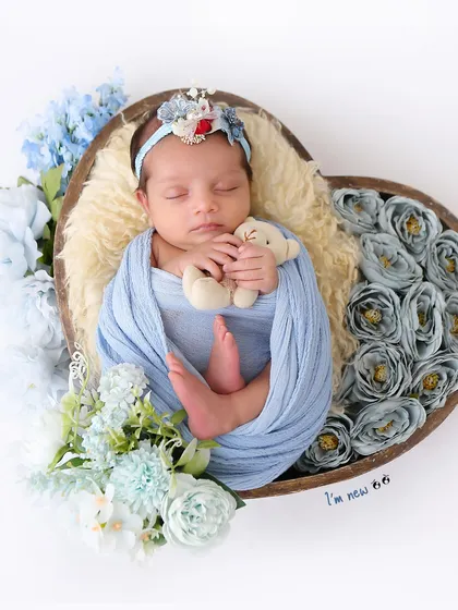 Holding a tiny teddy bear while sleeping, this newborn is surrounded by blue flowers in a heart-shaped prop. These small details add so much charm.
