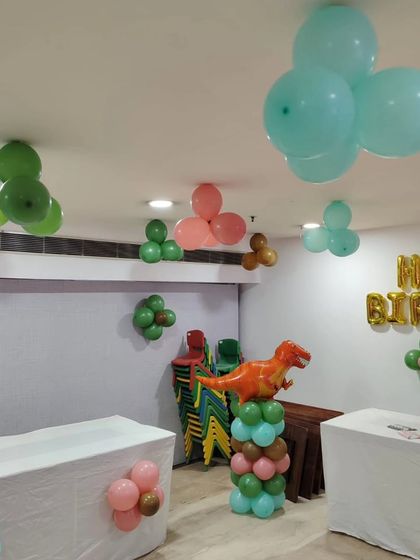 A full view of the party space, showcasing the dinosaur balloon pillar, 'Happy Birthday' foil letters, and ceiling balloon decor that transformed the room into a Jurassic playground.