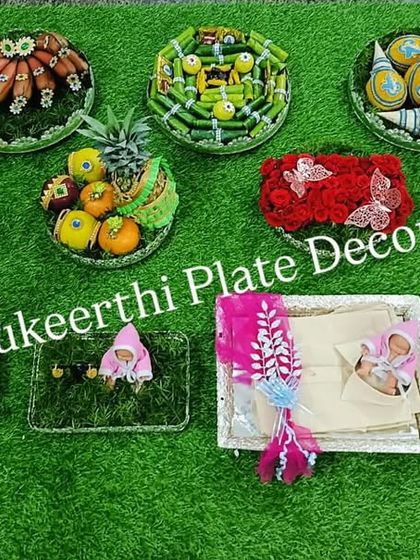 A top-down view of platters prepared for an ear-piercing ceremony in Karur. This shows the creative arrangements of fruits, sweets, and thematic dolls.