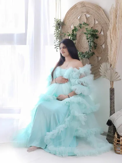 Soft, dreamy, and ethereal. This mom-to-be looks serene in a light blue ruffled gown, posed near a window to capture the soft natural light.