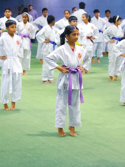 A young girl with a purple belt stands in a ready stance, showcasing her progress and confidence gained through our karate program.
